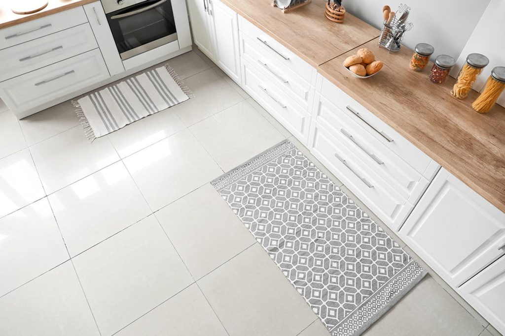 Modern kitchen floor featuring glossy tile, decorative grey runner rug, wooden countertop, and kitchen appliances, illustrating tile flooring options for homeowners.
