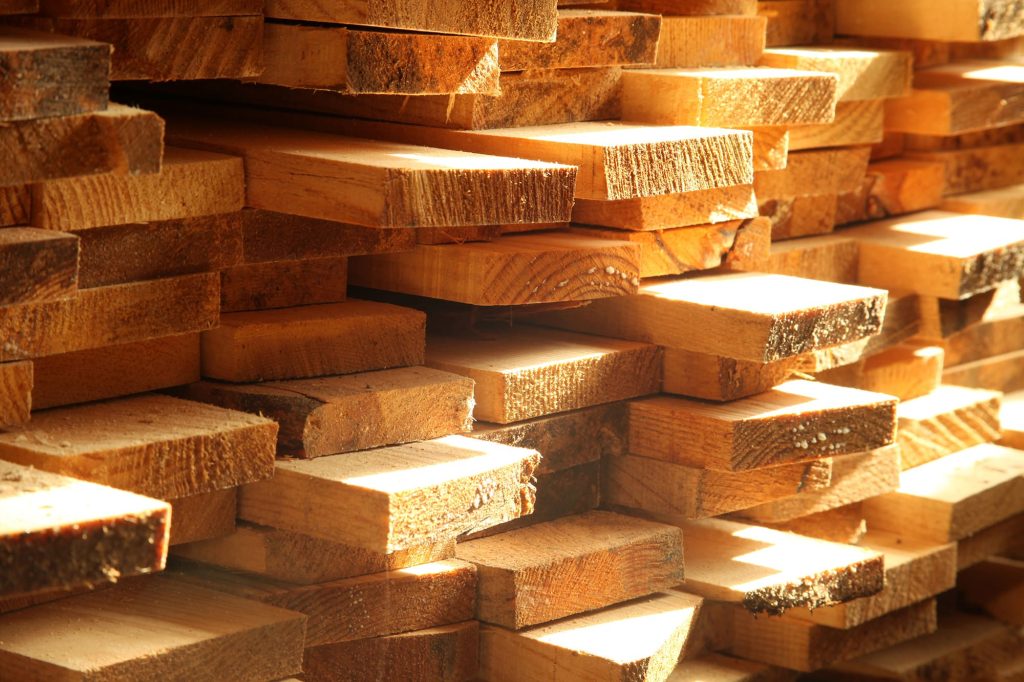Different types of lumber stacked in sunlight, highlighting textures and colors, relevant for outdoor decking and home improvement projects.