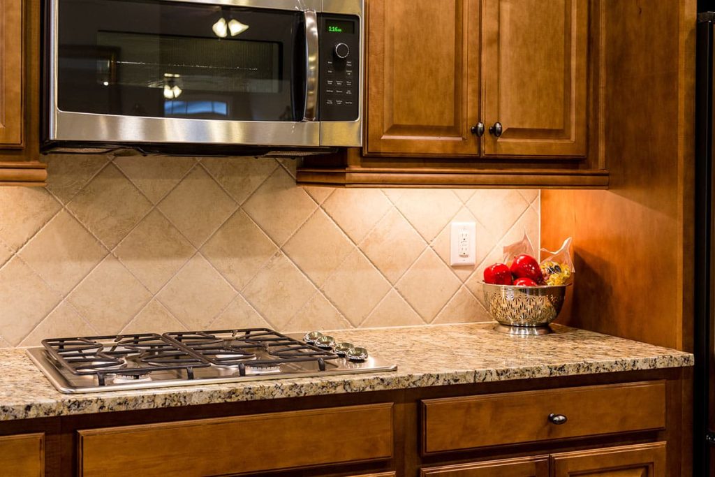 Kitchen countertop with granite surface, gas stove, modern microwave, and decorative bowl of red apples, showcasing cabinetry design and functionality for home improvement projects.